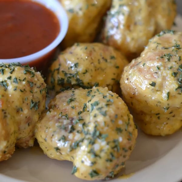 Golden-brown garlic knots, coated in melted cheese and herbs, with a side of marinara sauce.