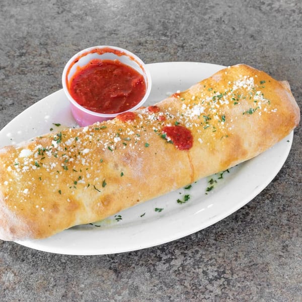 A golden-brown calzone from Ray's Pizza, topped with parmesan and parsley, served with a side of marinara sauce.