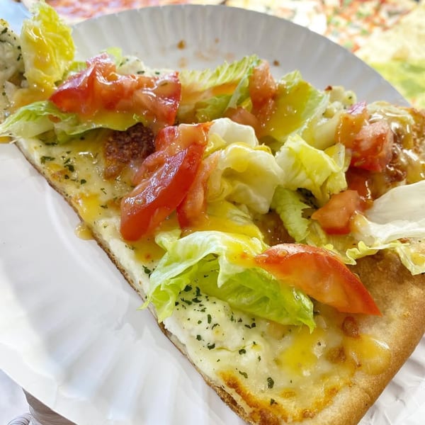 A slice of Ray's Pizza with melted cheese, fresh lettuce, diced tomatoes, and a drizzle of dressing.