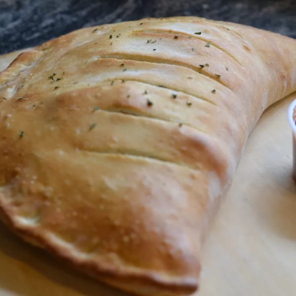 A golden-brown calzone from Ray's Pizza, sprinkled with herbs, rests on a light surface.